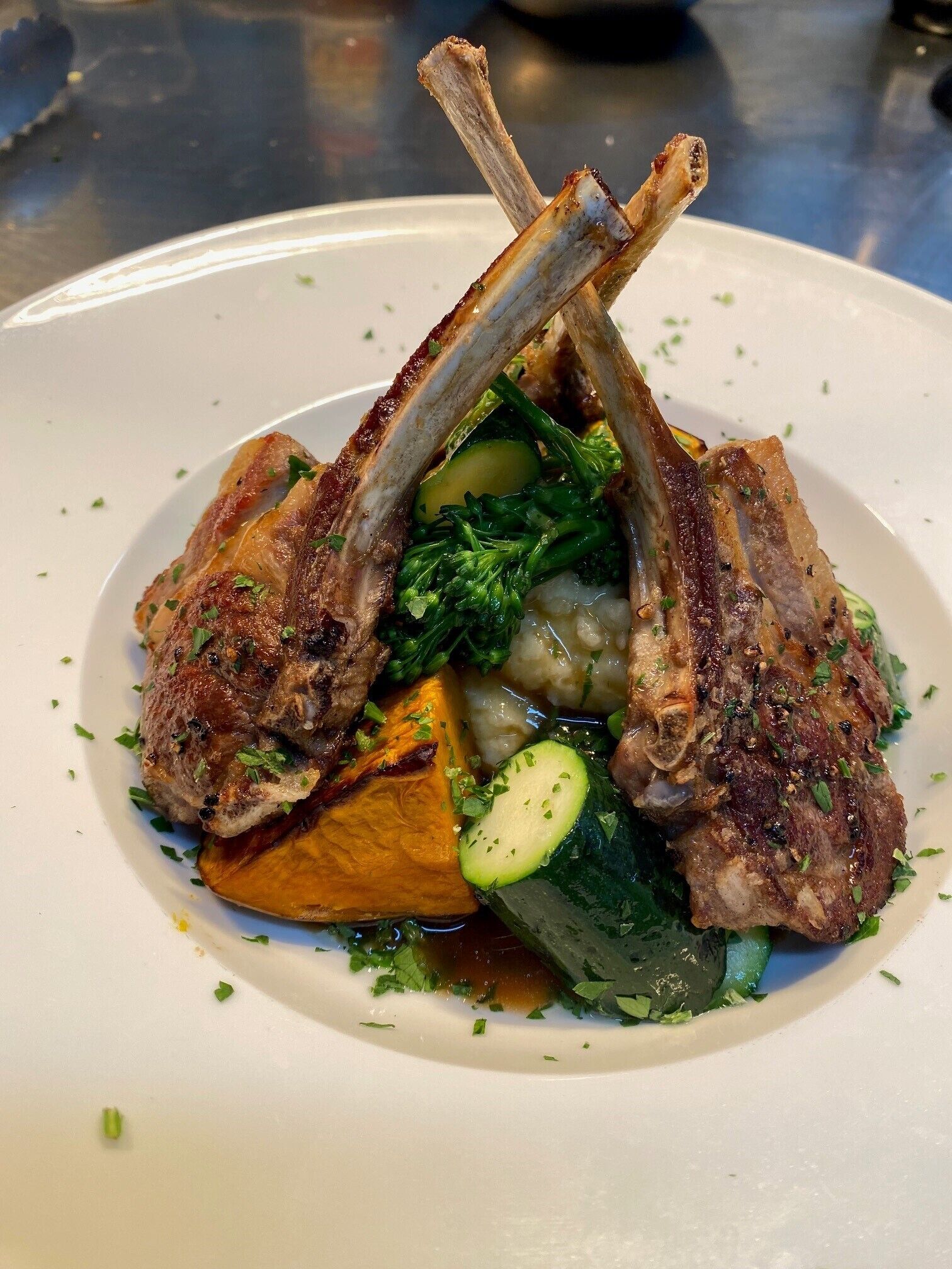 A plate with grilled lamb chops, vegetables, and a sauce.