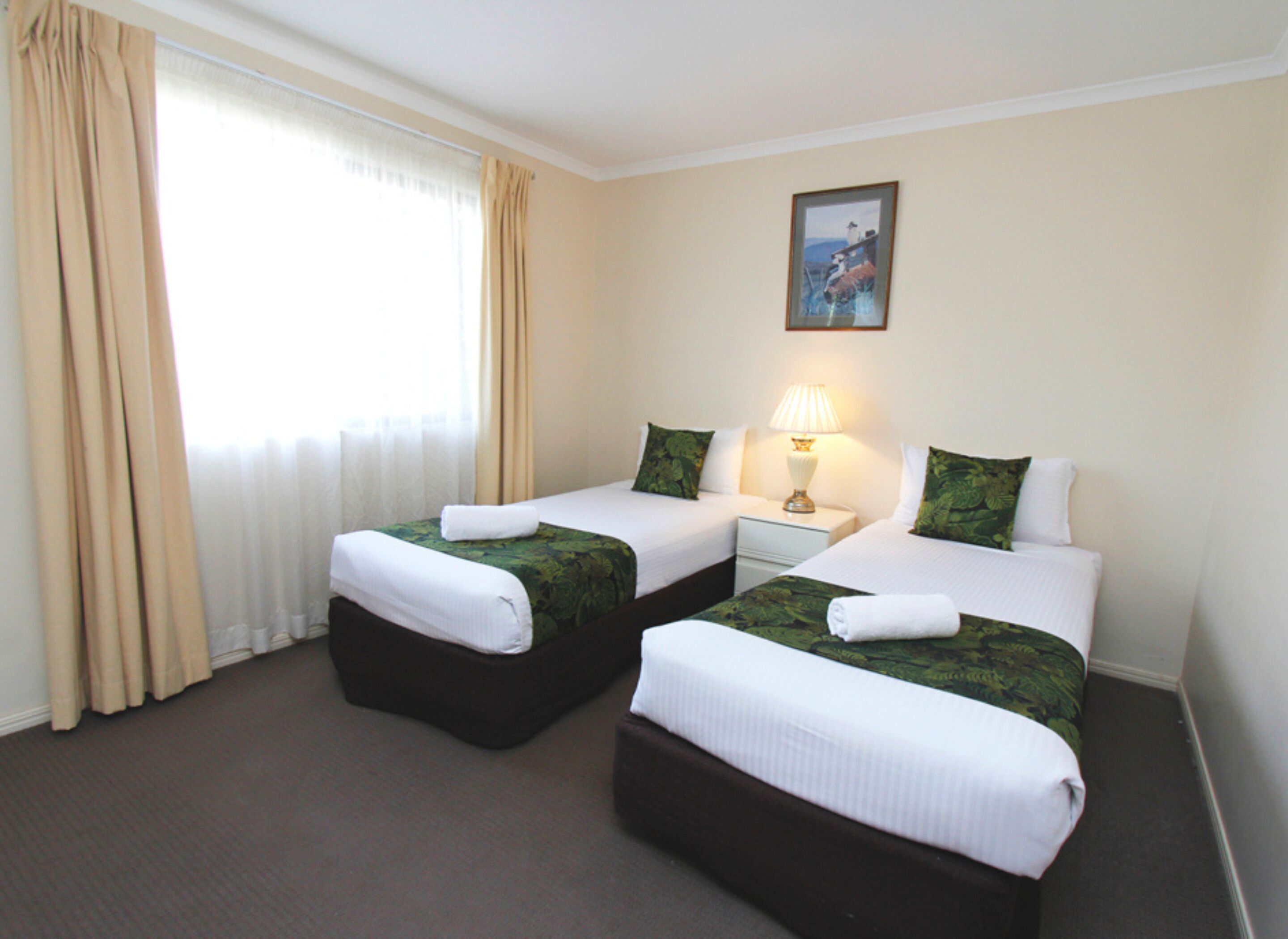A hotel room with two beds, a nightstand with a lamp, and a painting on the wall.