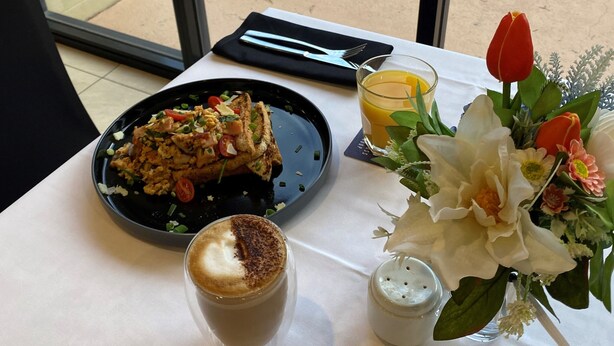 Ein Esstisch mit Mahlzeit, einem Glas Saft und einer Blumenkomposition.