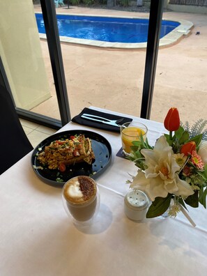 A dining table with a meal, a glass of juice, and a flower arrangement. - The Palms Motel (Chinchilla)