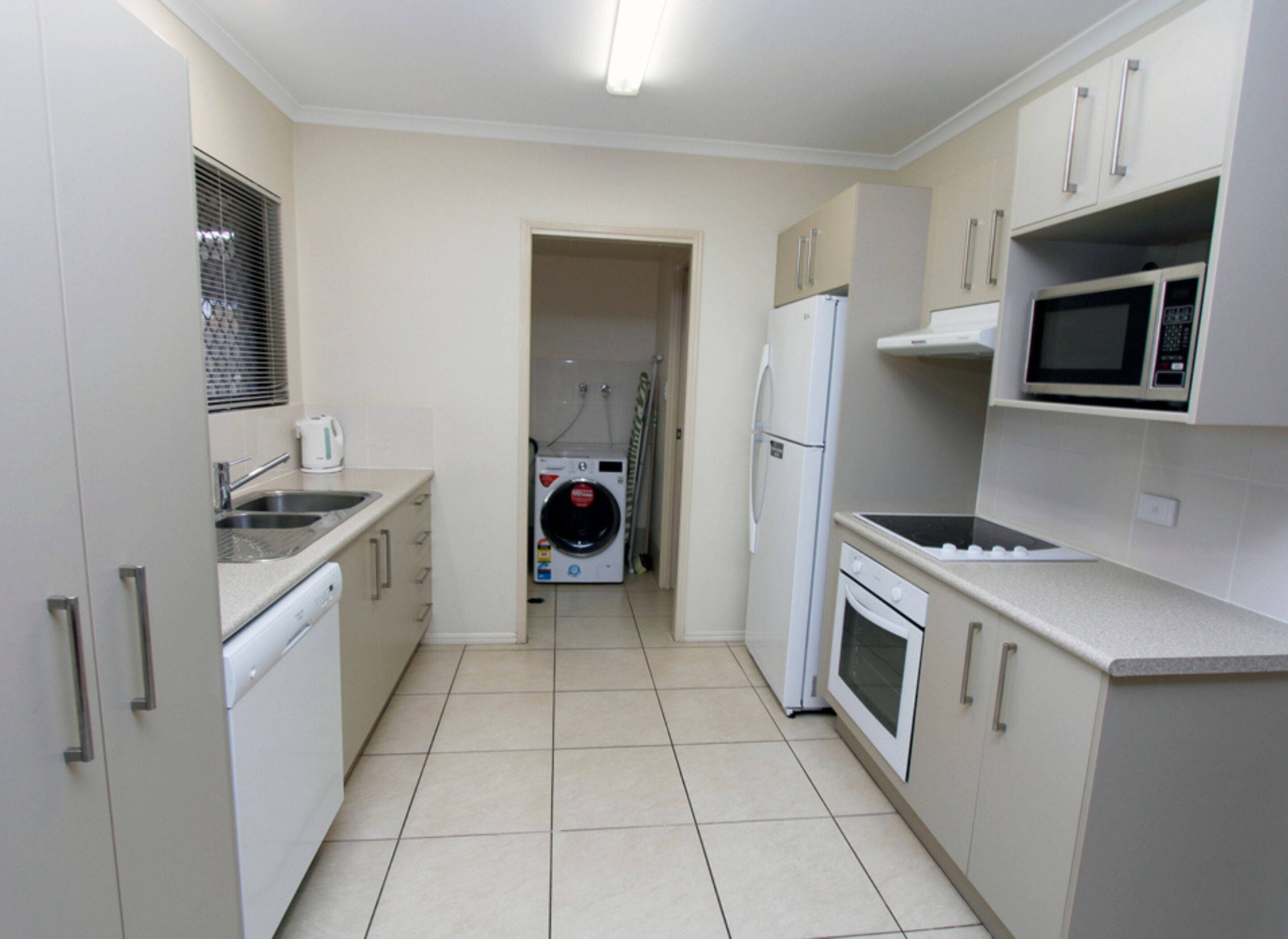 A compact kitchen with a washing machine, a refrigerator, a microwave, and a sink.