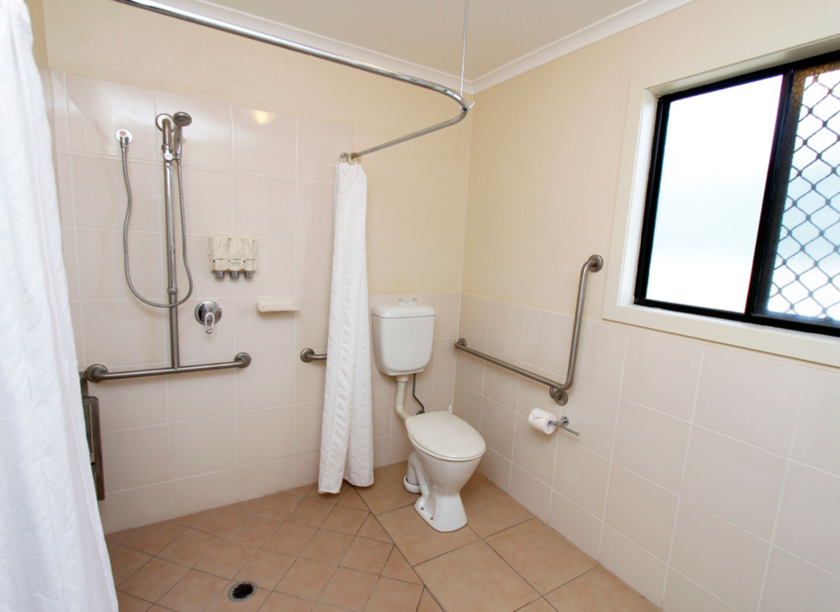 A bathroom with a toilet, shower, grab bars, and a window.