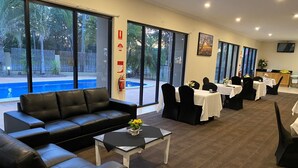 Eine Hotelhalle mit Blick auf einen Pool, mit Ledersofas, Tischen und Esstischen mit Stühlen.