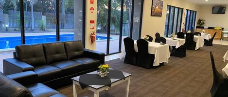 Vestíbulo de hotel con vista a la piscina, sofás de cuero, mesas y mesas de comedor con sillas.