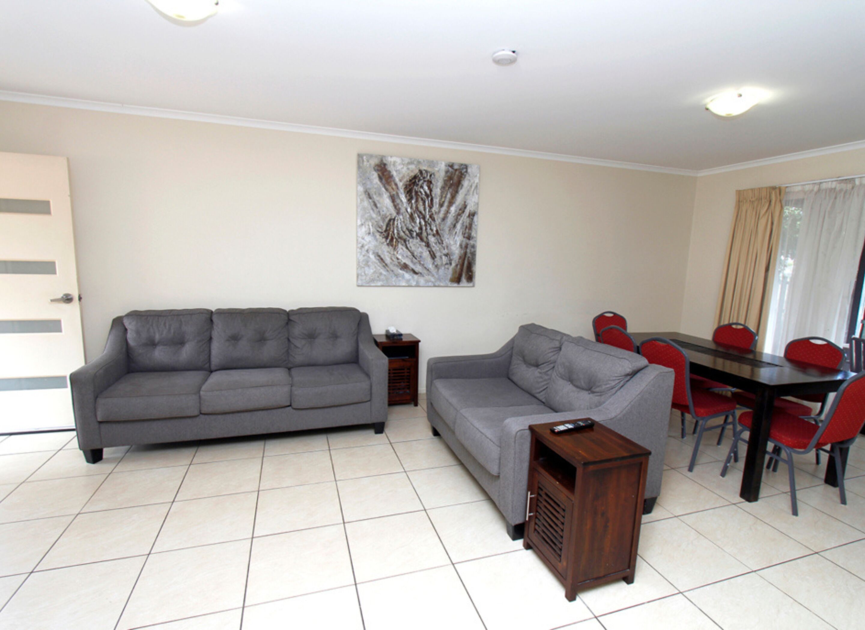 A living room with two grey sofas, a wooden side table, and a dining area with a table and red chairs.