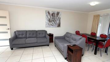 A living room with two grey sofas, a wooden side table, and a dining area with a table and red chairs.
