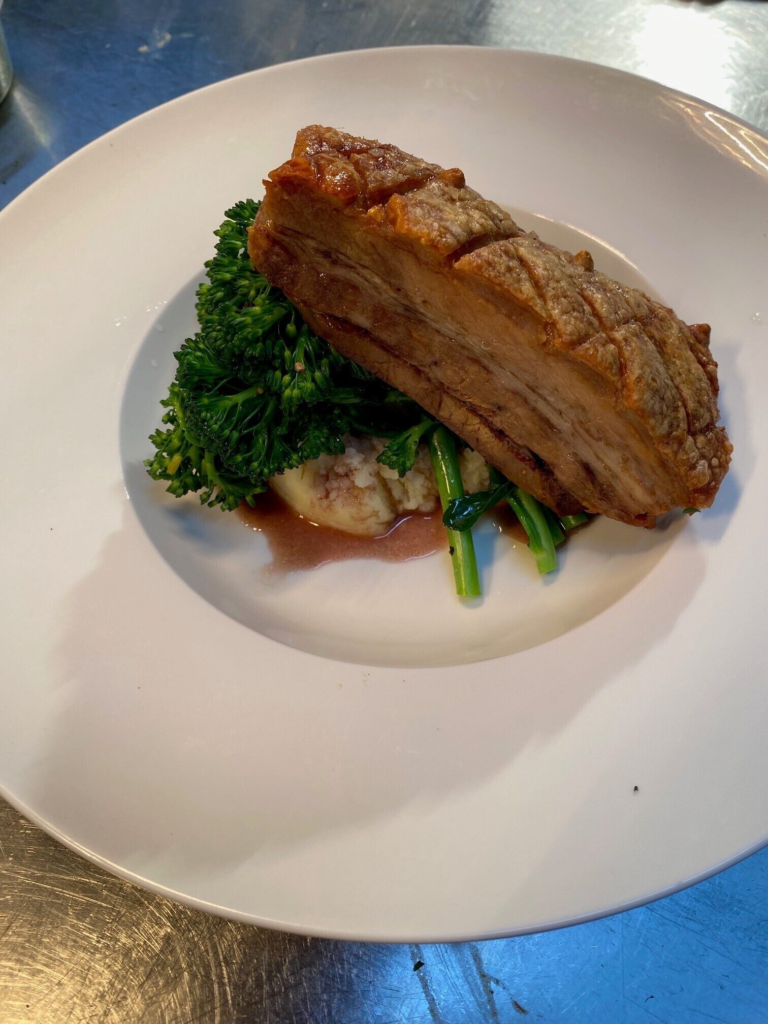 A plate with a piece of meat, broccoli, and mashed potatoes.
