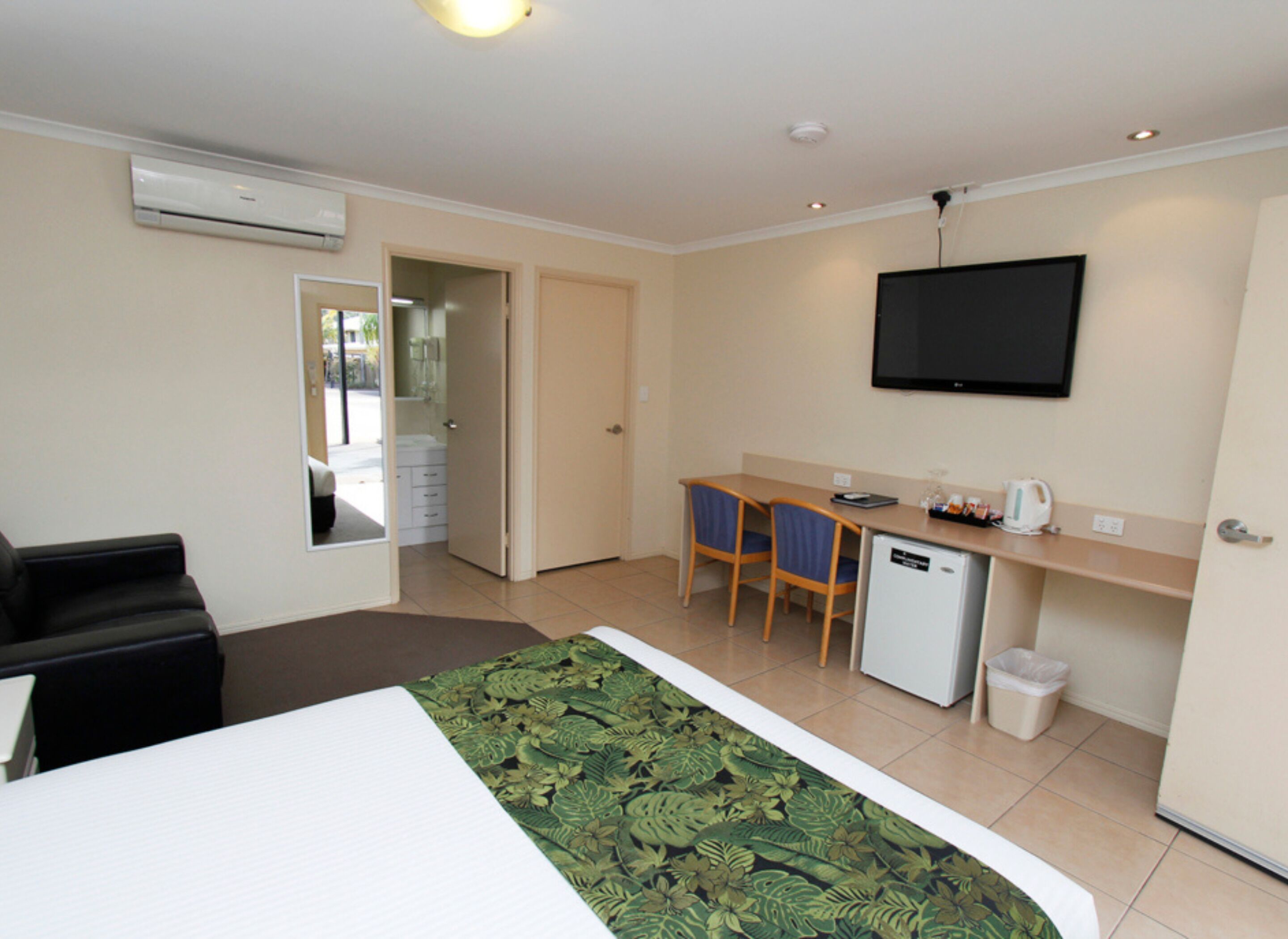 A hotel room with a bed, a desk, chairs, a television, and a small refrigerator.