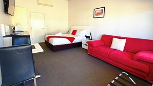 A hotel room with a bed, a red sofa, a desk with a computer, and a TV mounted on the wall. - Gunnedah Lodge Motel (Gunnedah)