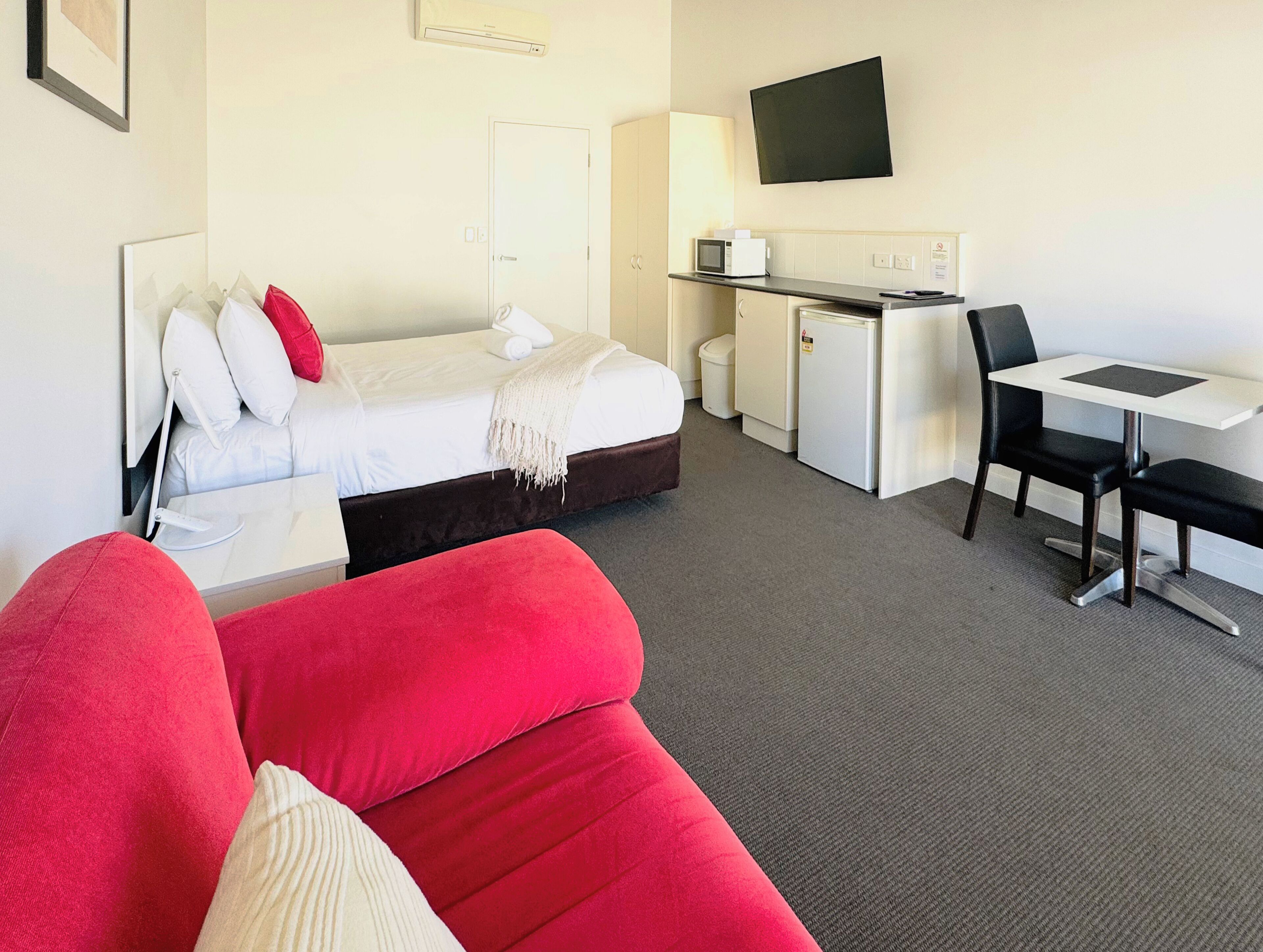 Habitación de hotel con cama, escritorio, silla y televisor en la pared.