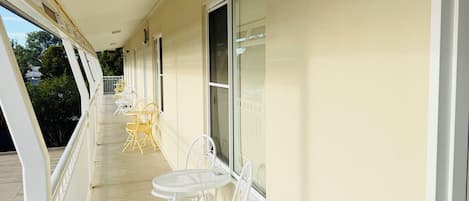 Un balcon abrité, doté de chaises et de tables en métal blanc, d’une balustrade blanche et d’un mur de couleur beige.