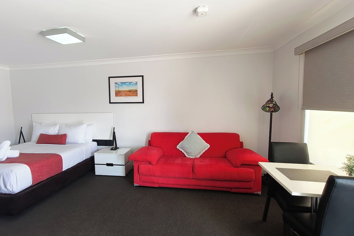A hotel room with a bed, a red sofa, a desk, and a picture on the wall.