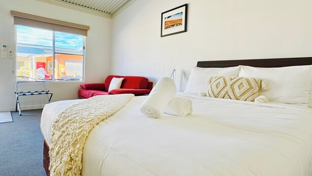 A hotel room with a large bed, a red chair, a window with a view, and a framed picture on the wall. - Gunnedah Lodge Motel (Gunnedah)
