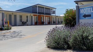 A motel with a central building and a smaller attached structure, featuring a covered outdoor seating area and a sign indicating the motel's direction. - Gunnedah Lodge Motel (Gunnedah)