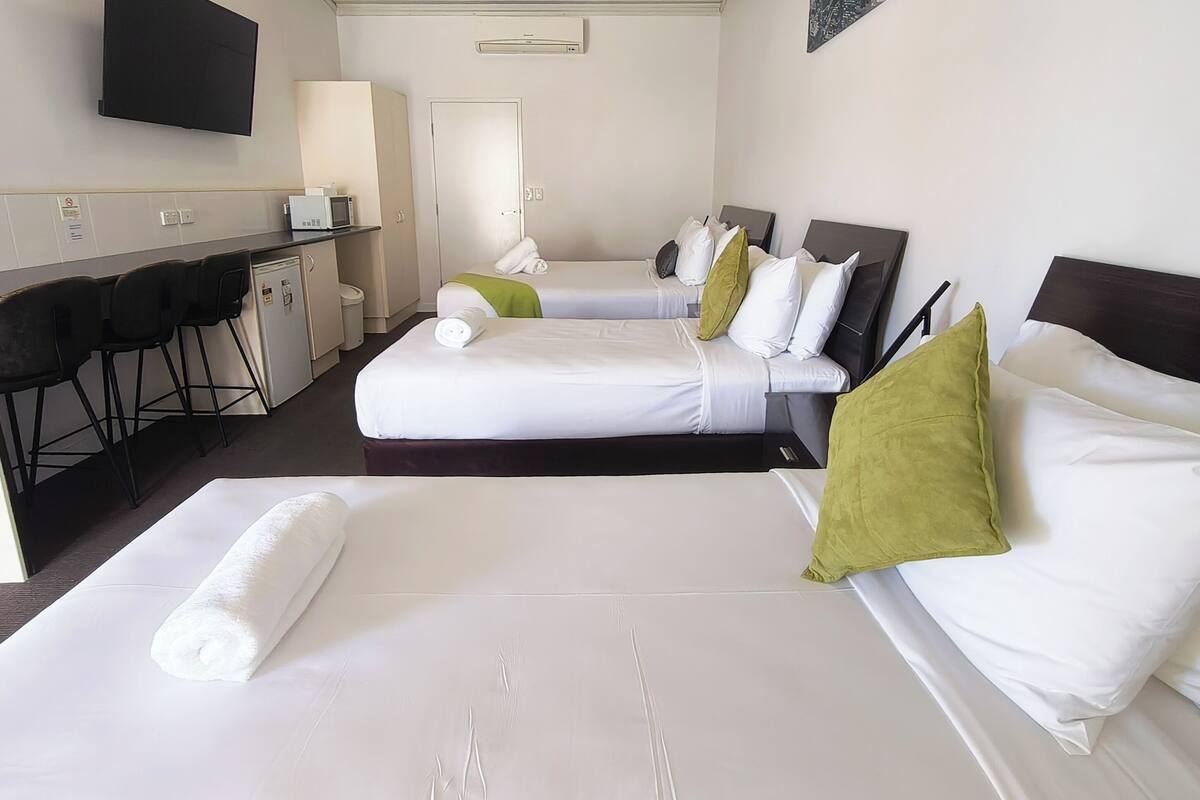 A hotel room with two beds, a desk with a microwave, chairs, and a TV mounted on the wall.