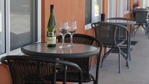A table with a bottle of wine and two glasses on a balcony with wicker chairs. - Gunnedah Lodge Motel (Gunnedah)