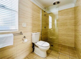 Un baño con inodoro, ducha con mampara de vidrio, toallero y soporte para papel higiénico.