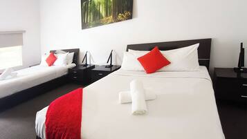 Une chambre d’hôtel avec deux lits, chacun agrémenté de draps blancs et d’oreillers rouges, une grande peinture représentant une forêt et un lit soigneusement fait avec une serviette roulée.