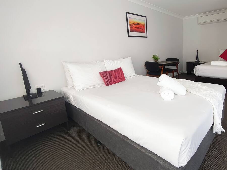 Ein Hotelzimmer mit Bett, Schreibtisch, Stuhl, kleinem Tisch, Pflanze und einem Bild an der Wand.