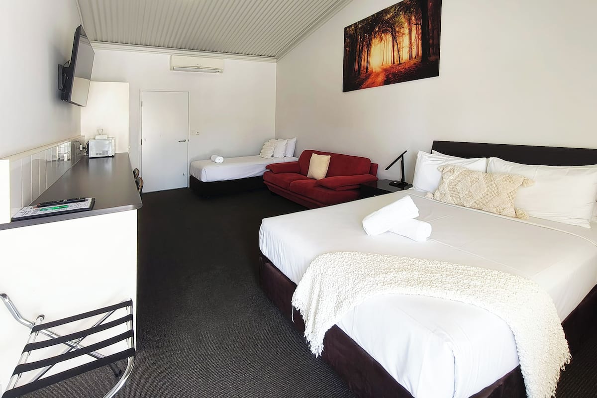 A hotel room with a bed, a red couch, a desk with a computer, and a TV mounted on the wall.