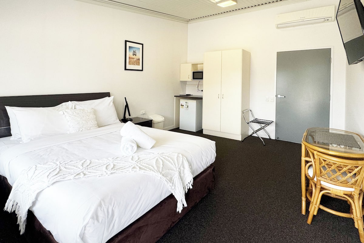 A hotel room with a bed, a desk with a chair, a television, and a wardrobe.