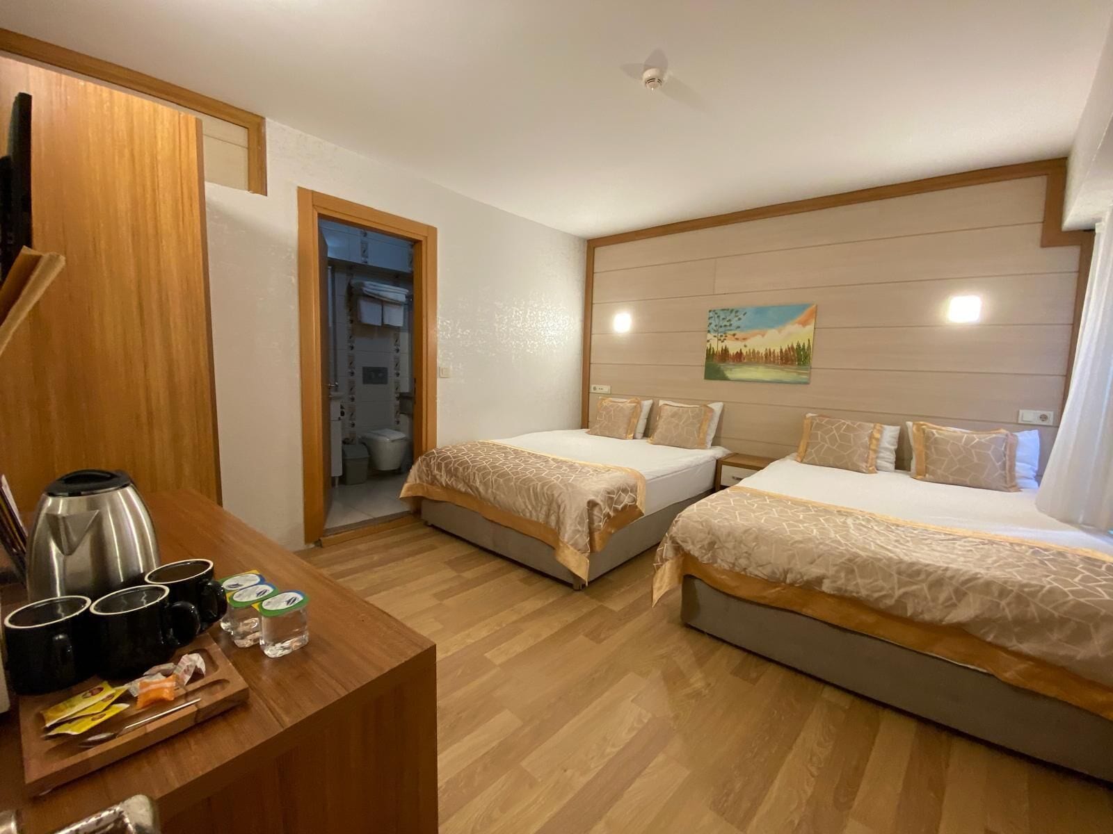 A hotel room with two beds, a wooden desk with a coffee maker, cups, and a tray of snacks.