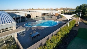 A modern outdoor swimming pool with a unique design, surrounded by a wooden deck and shaded by a white canopy. - Broadbeach Inverloch Resort (Inverloch)