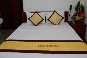A hotel bed with a yellow and brown bedspread, two decorative pillows, a bedside table with a phone, and a floral arrangement. - Golden Beach Hotel (Da Nang)