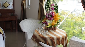Une chambre d’hôtel avec une table à manger dressée pour deux personnes, une chaise en osier, un miroir et une fenêtre avec des rideaux.