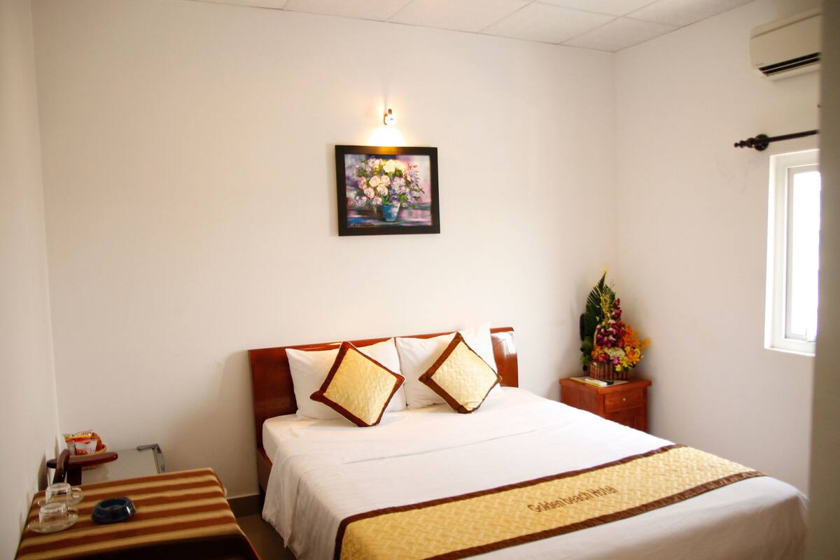 A hotel room with a bed, a bedside table with a lamp, a small table with a glass and a bowl, and a wall-mounted picture.