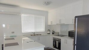 A modern kitchen with white cabinets, a central island, a microwave, and a dishwasher. - Halls Gap Valley Lodges (Halls Gap)