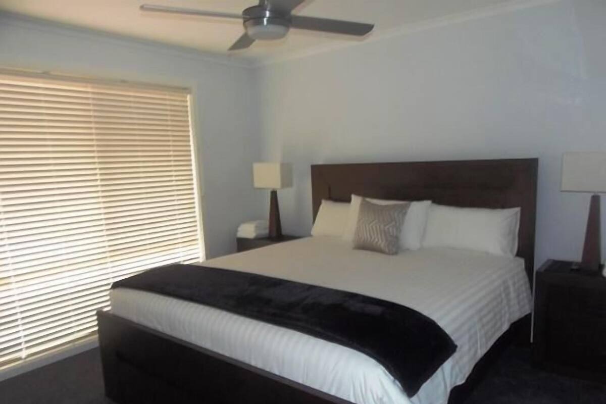 A bedroom with a bed, a ceiling fan, a nightstand, and a window with blinds.