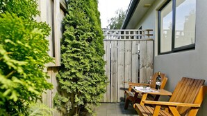 Un patio con una mesa y sillas de madera, una valla de madera y un árbol alto.