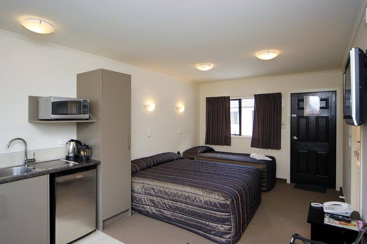 A compact hotel room with a kitchenette, a bed, a desk, and a TV.
