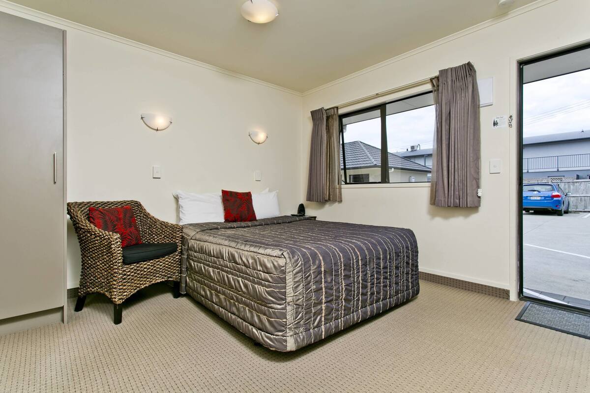 A bedroom with a bed, a chair, a window with curtains, and a view of the outside.