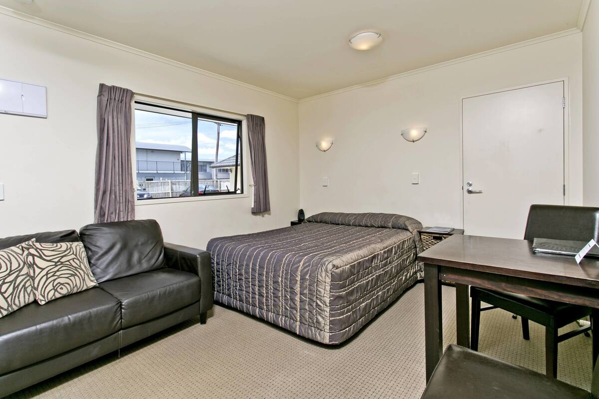 A hotel room with a bed, a desk, a chair, a sofa, and a window with curtains.