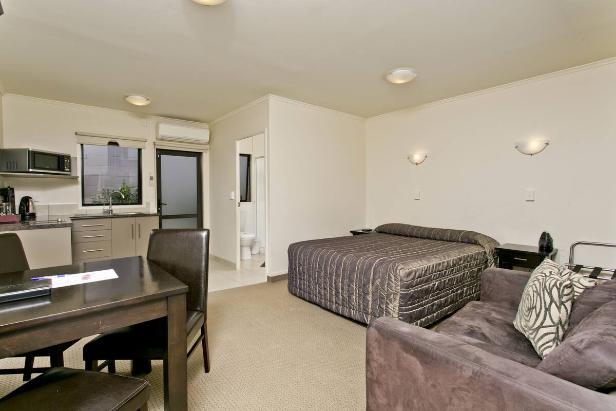 A compact hotel room with a kitchenette, a bed, a sofa, and a desk.