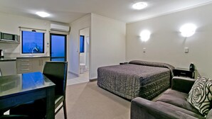 Una habitación compacta con cama, sofá, mesa de comedor y kitchenette.