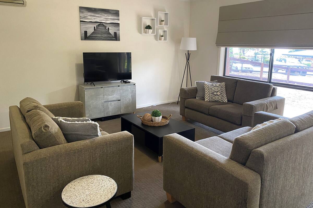 A living room with a sofa set, a coffee table, a TV, and a window with a view of a parking lot.