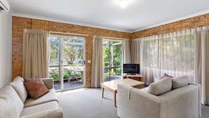A living room with a brick wall, a sofa, a television, and a sliding glass door leading to an outdoor area. - Mansfield Country Resort (Mansfield)