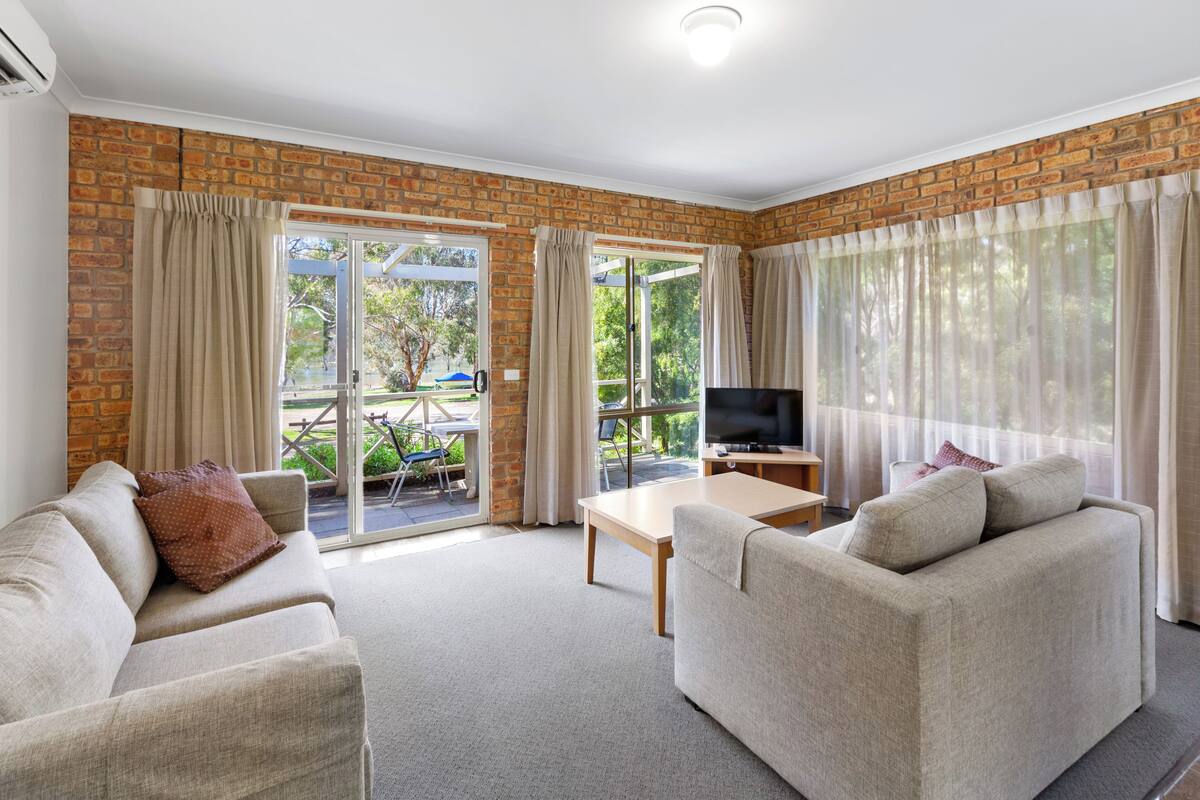 A living room with a brick wall, a sofa, a television, and a sliding glass door leading to an outdoor area.