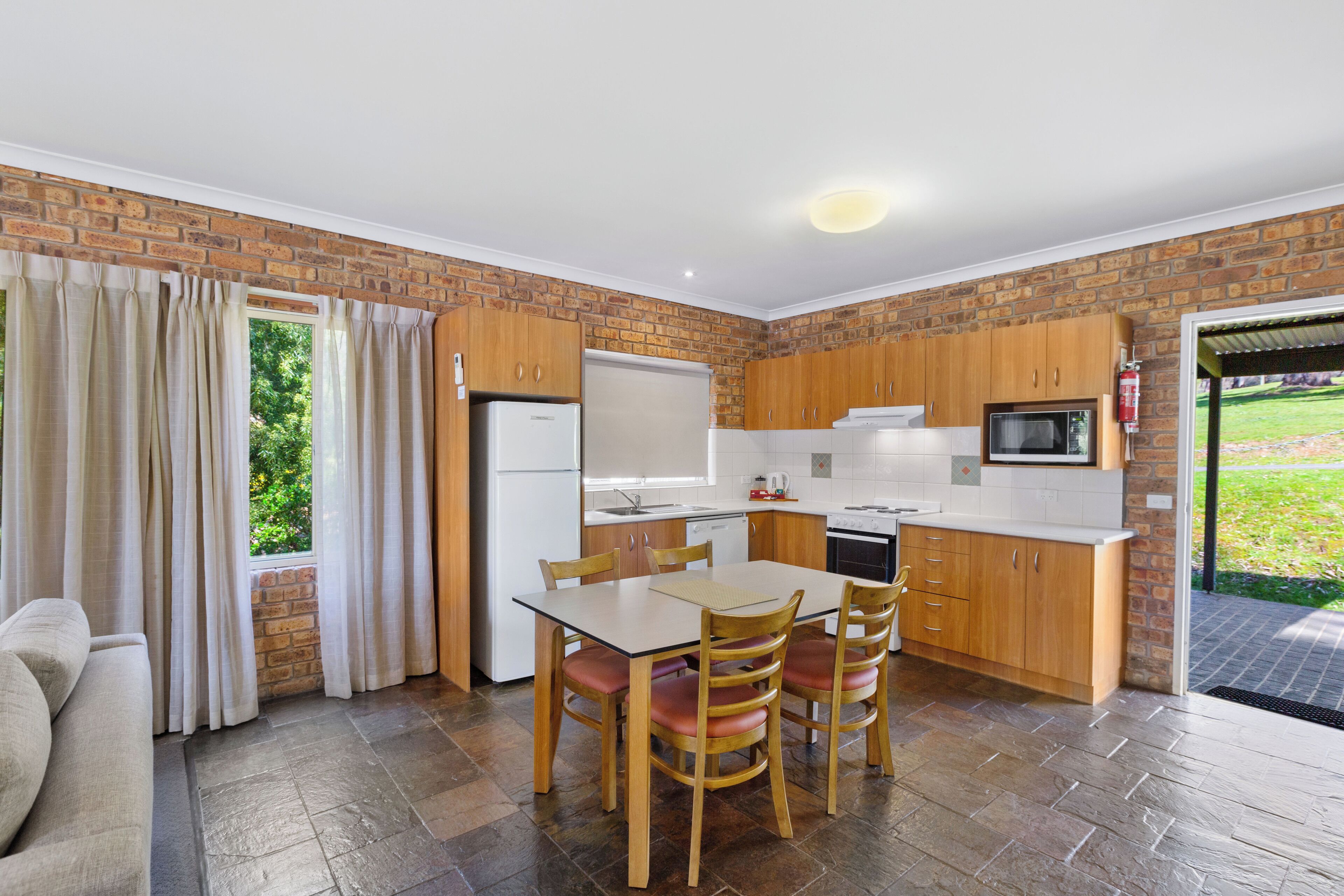 A modern kitchen with wooden cabinets, a dining table with chairs, and a refrigerator.