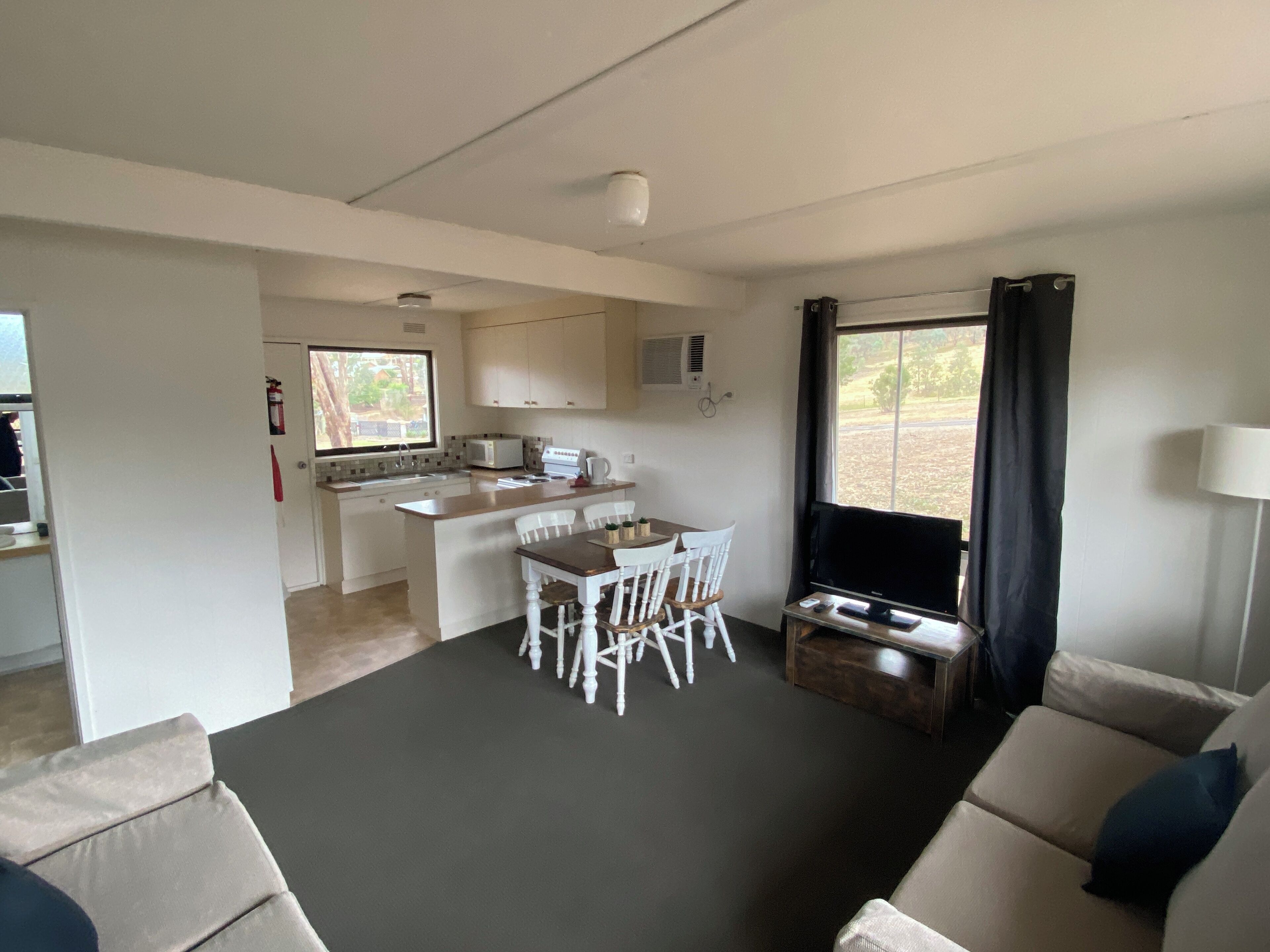 A compact living space with a kitchenette, a dining area with white chairs, a sofa, and a TV.