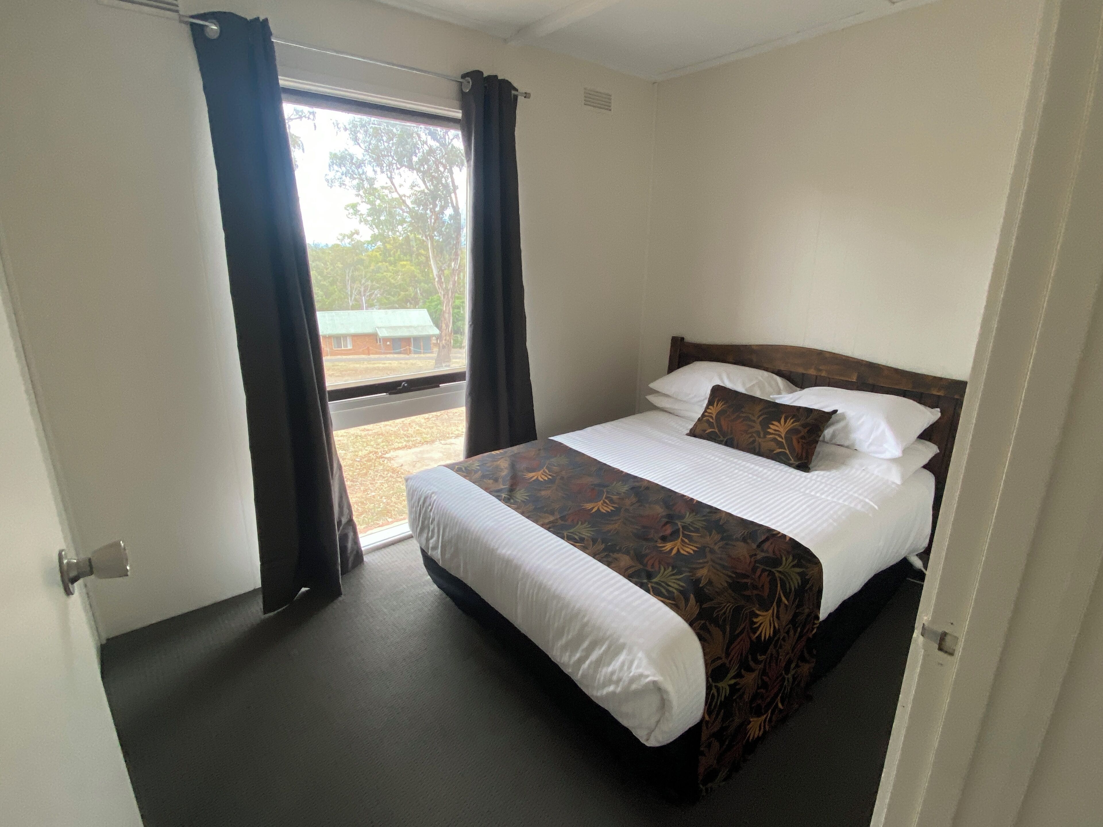 A hotel room with a bed, a window with curtains, and a view of the outside.