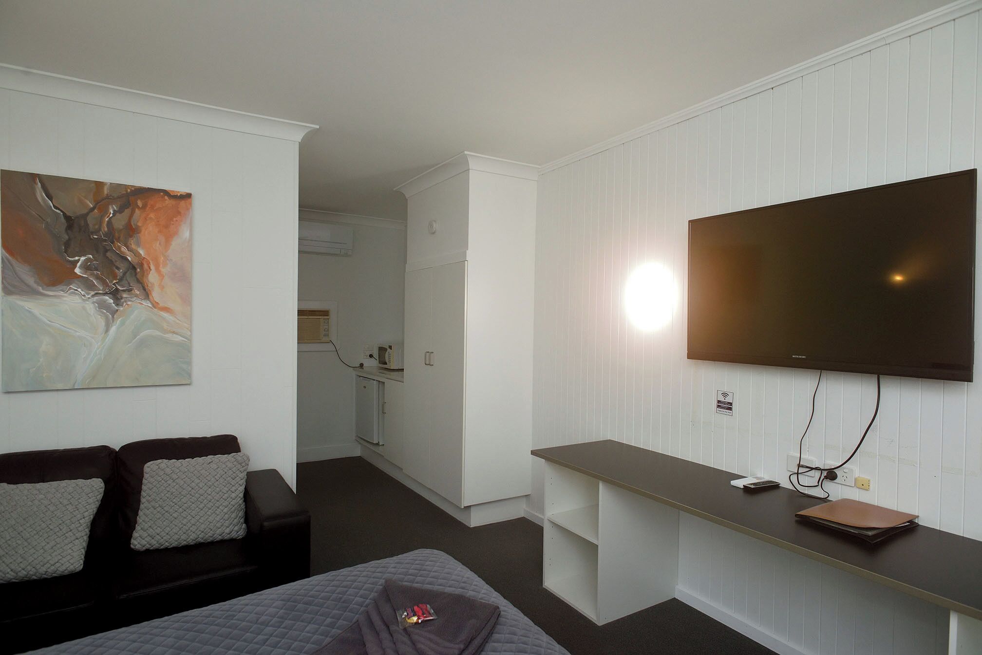 A hotel room with a bed, a desk, a television, and a painting on the wall.