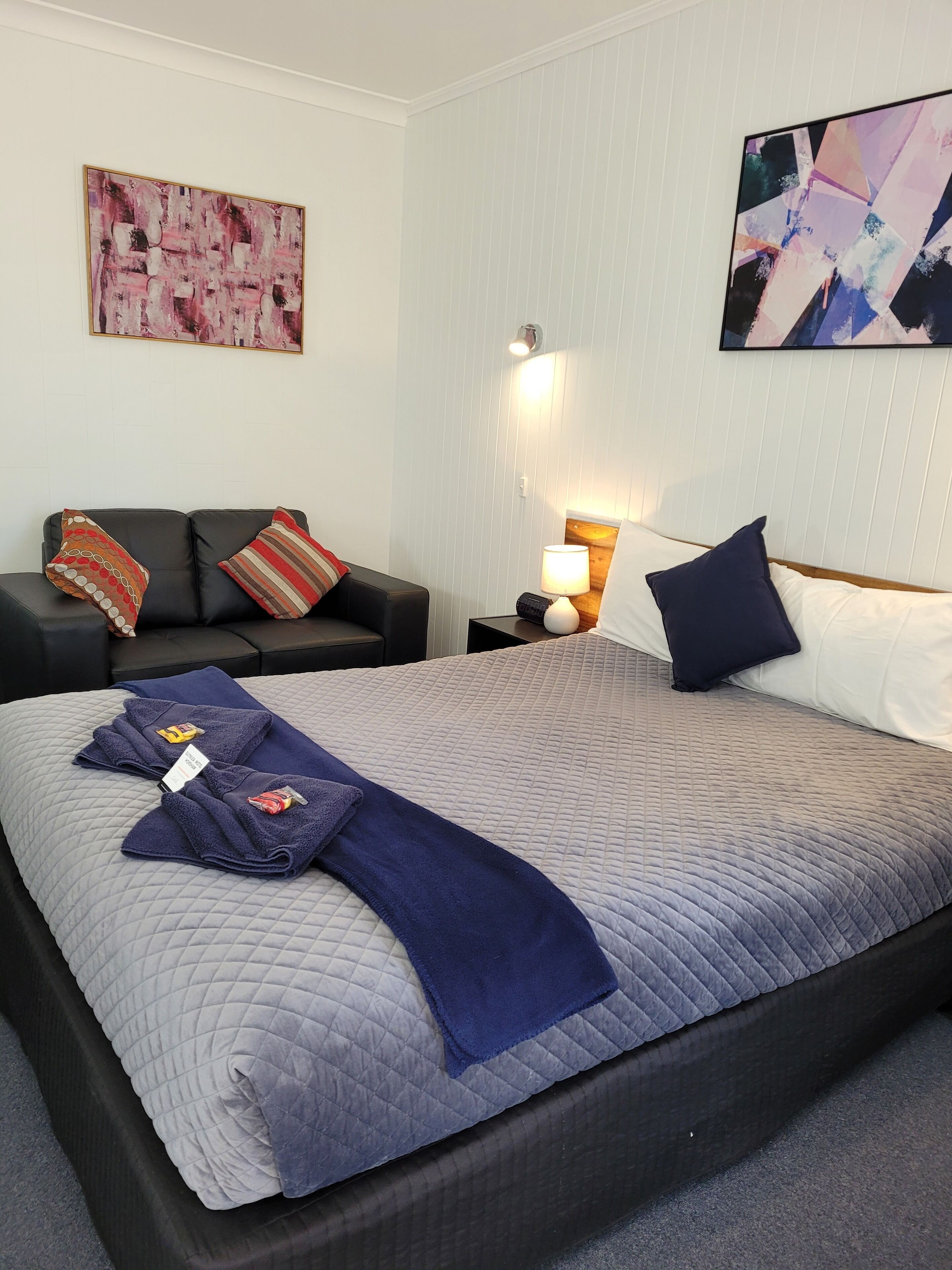 A neatly arranged hotel room with a bed, a sofa, and a nightstand with a lamp.