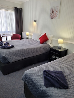 A hotel room with two beds, a desk, a chair, and a window with curtains.