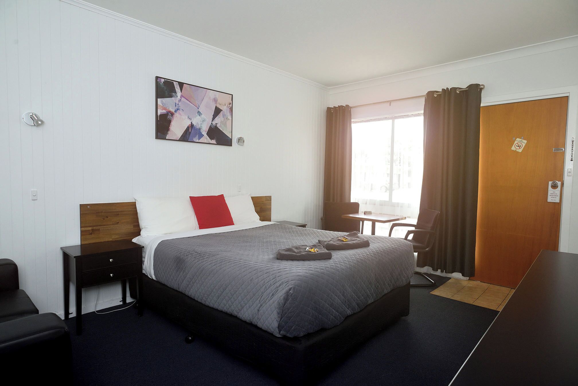 Une chambre d’hôtel avec un lit, un bureau, une chaise, une fenêtre avec des rideaux et un tableau au mur.