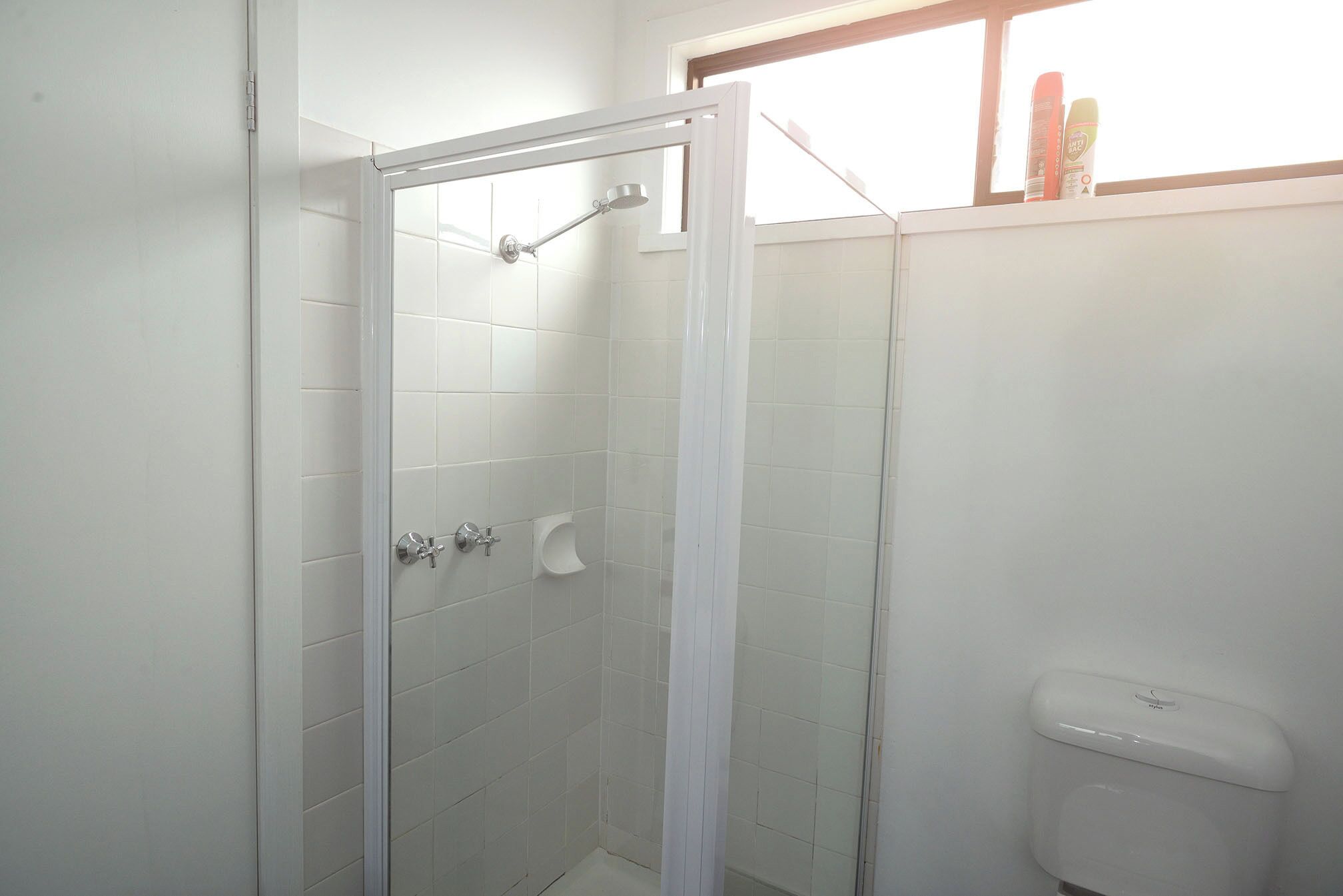 A bathroom with a glass-enclosed shower, a toilet, and a window above the toilet.