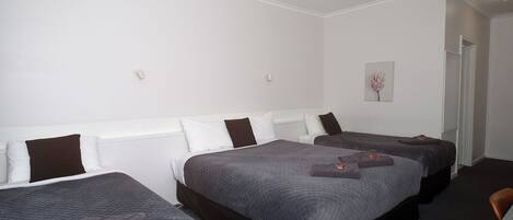 A hotel room with three beds, a small table, and a chair.
